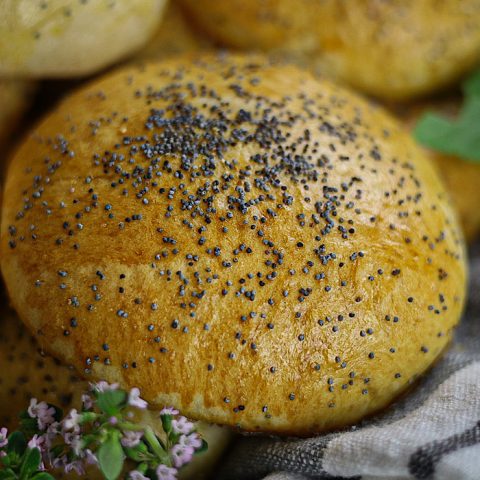 soft Buttery Sourdough Rolls or buns with poppy seeds on towel and herbs around