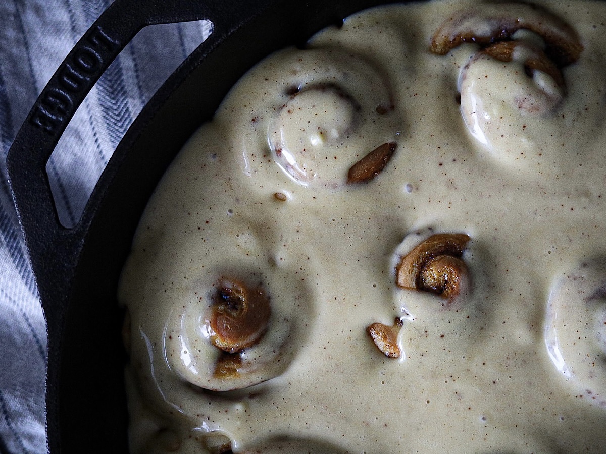 fluffy sourdough cinnamon rolls in skillet with cream cheese frosting