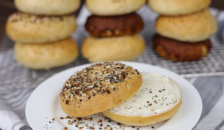 Sourdough bagel with cream cheese and bagels stacked in background