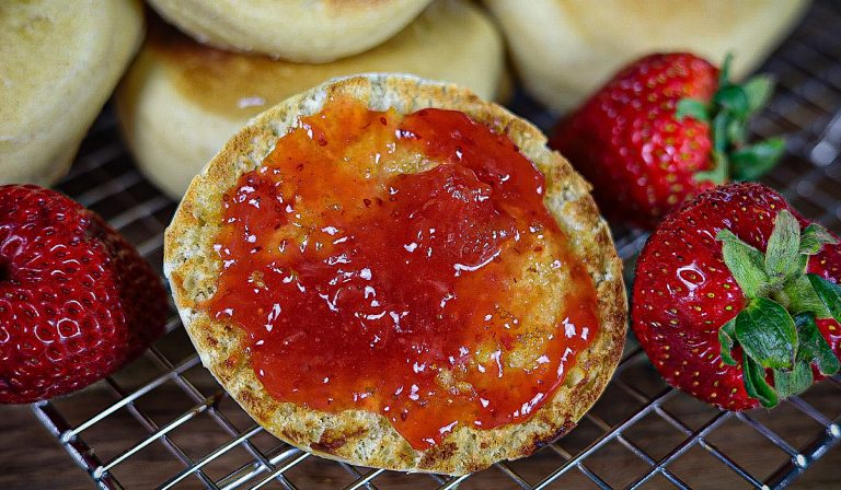 english muffin with strawberry jam on wire rack surrounded by strawberries