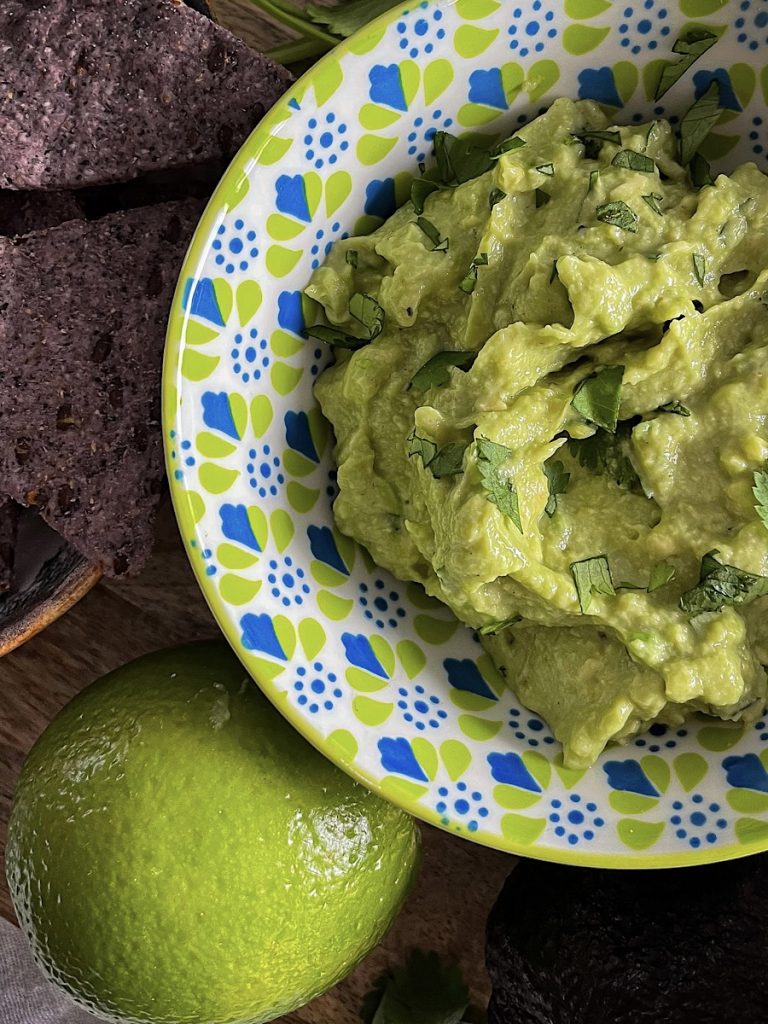 simple guacamole in green and blue bowl with chips, lime and cilantro