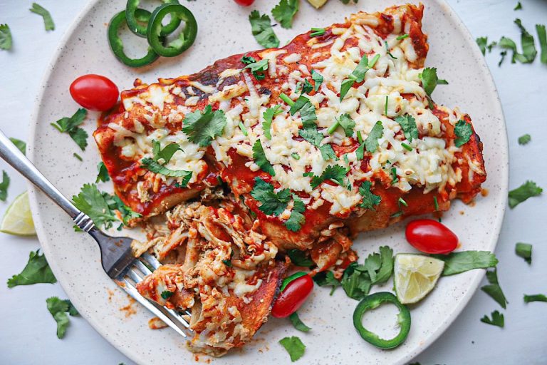 Simple Chicken enchiladas on plate with cilantro, fork, jalapenos, tomatoes, lime simple is gourmet